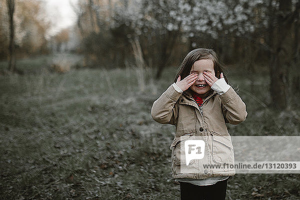 Girl crying while standing on grassy field in forest during winter