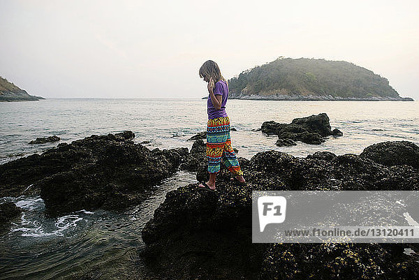 Seitenansicht eines am Ufer auf Felsen stehenden Mädchens