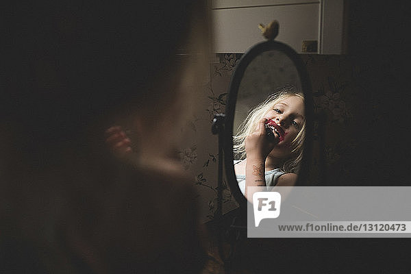Girl applying lipstick while looking in mirror at home