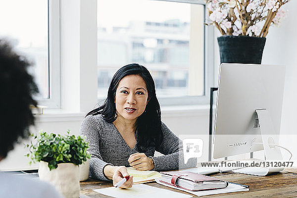 Businesswoman talking with female colleague while working at desk in office