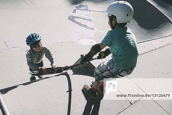 Brüder ziehen bei Sonnenschein Roller im Skateboard-Park