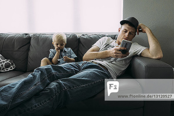 Vater telefoniert  während der Sohn zu Hause auf dem Sofa sitzt