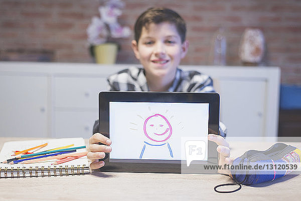 Porträt eines lächelnden Jungen  der zu Hause auf einem Tablet-Computer zeichnet