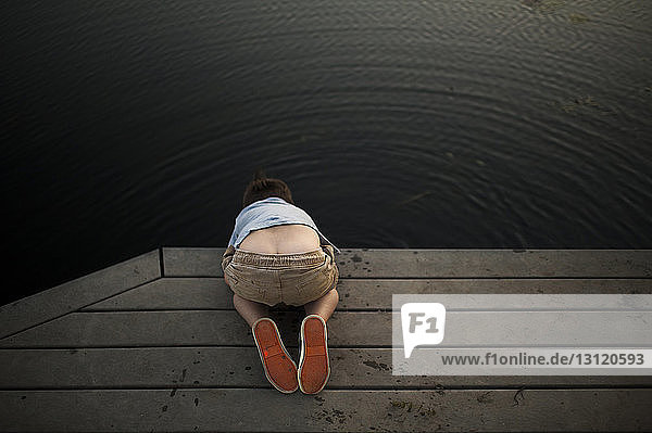 High angle view of boy looking in lake while kneeling on pier at park