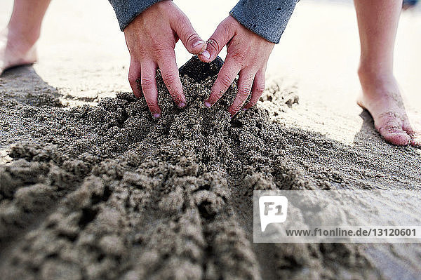 Ausgeschnittenes Bild eines Jungen  der am Strand mit Sand spielt