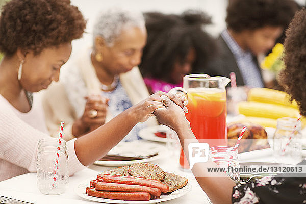 Familie hält beim Gebet am Frühstückstisch Händchen
