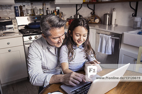 Hochwinkelaufnahme von Vater und Tochter am Laptop in der Küche zu Hause