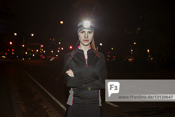 Portrait of confident woman wearing illuminated headlamp while standing on street at night