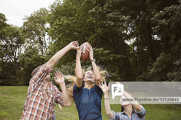 Playful friends catching football ball on grassy field
