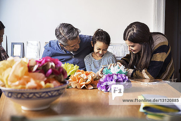 Father and mother with daughters making paper flowers at table