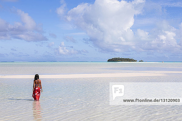 Rückansicht einer Frau in Sharong  die in der Lagune von Aitutaki gegen den Himmel steht