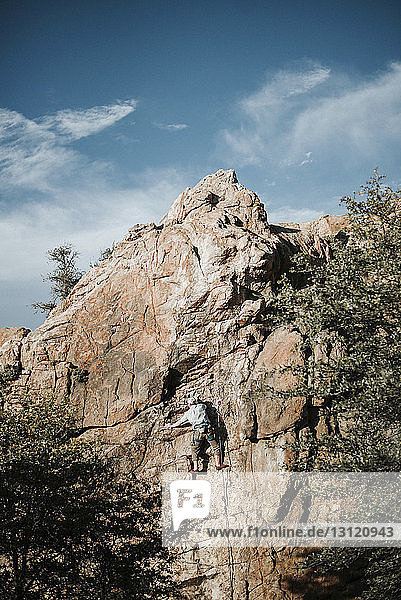 Low angle view of man climbing rock against sky during sunny day