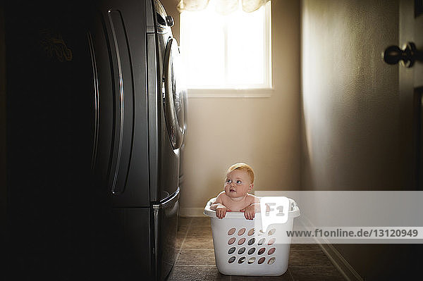 Kleiner Junge ohne Hemd im Wäschekorb,  der die Waschmaschine anschaut