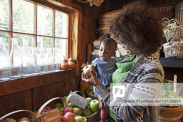Mother showing apple to baby daughter in organic shop