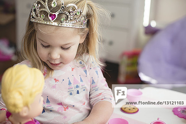 Mädchen trägt Krone beim Spielen mit Puppe zu Hause