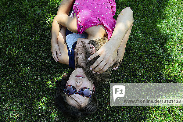 Draufsicht einer Mutter  die ihre Tochter umarmt  während sie auf einem Grasfeld liegt