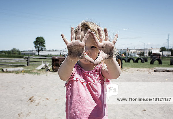 Portrait of girl showing dirty hands while standing on sand against clear sky at playground