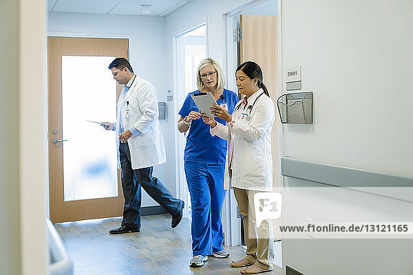 Female doctors discussing over tablet computer while male colleague walking by in hospital