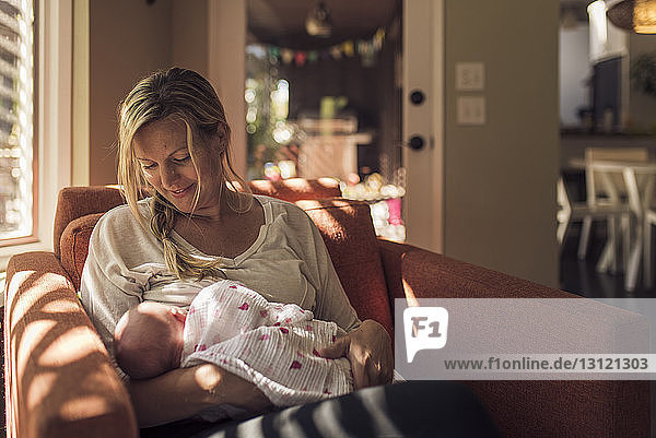 Mother looking at newborn daughter while relaxing on chair at home
