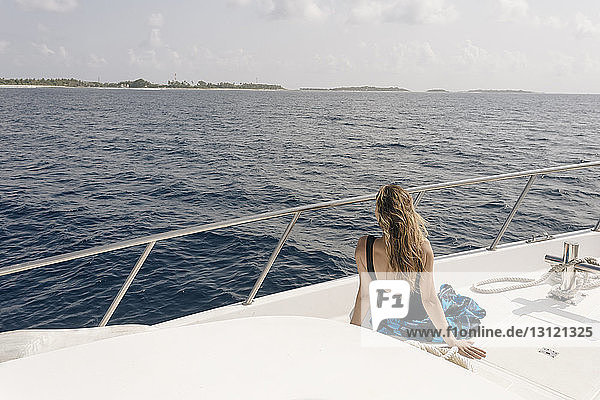 Rückansicht einer Frau  die bei sonnigen Tagen auf das Meer schaut  während sie mit einer Yacht gegen den Himmel fährt