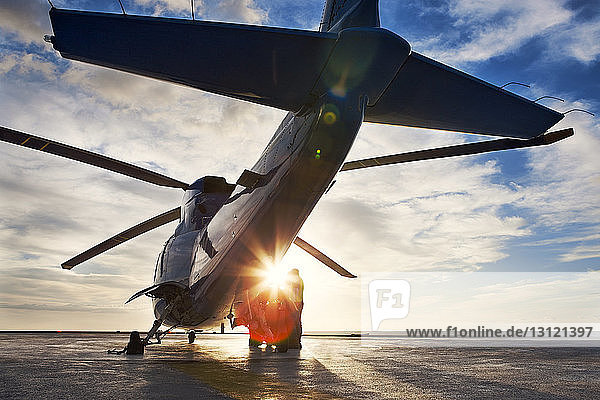 Hubschrauber von Arbeitern  die bei Sonnenuntergang auf dem Hubschrauberlandeplatz gegen den Himmel stehen