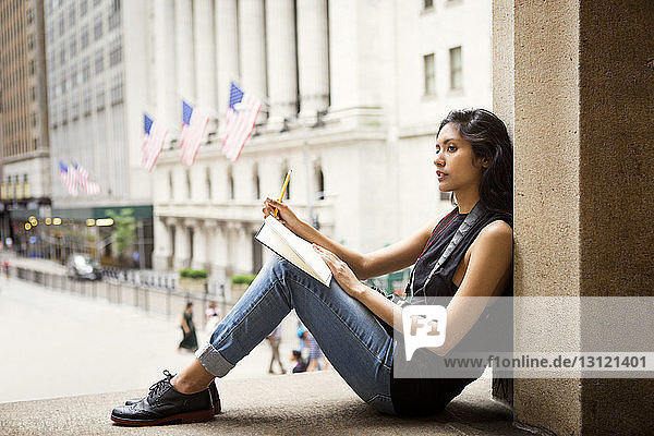 Nachdenkliche Frau schreibt in Buch  während sie auf Stufen in der Stadt sitzt