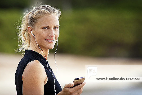 Porträt einer lächelnden Frau  die über ein Smartphone Musik hört
