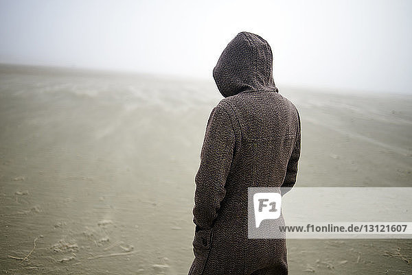 Frau mit Kapuzenmantel am Strand bei nebligem Wetter