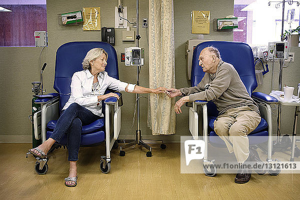 Senior couple holding hands while sitting on chairs in hospital