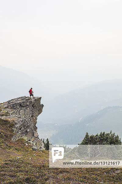 Seitenansicht eines Wanderers  der bei nebligem Wetter auf einer Klippe gegen Berge und Himmel steht
