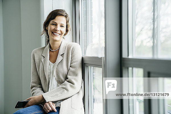 Porträt einer lächelnden Geschäftsfrau  die im Büro am Fenster sitzt
