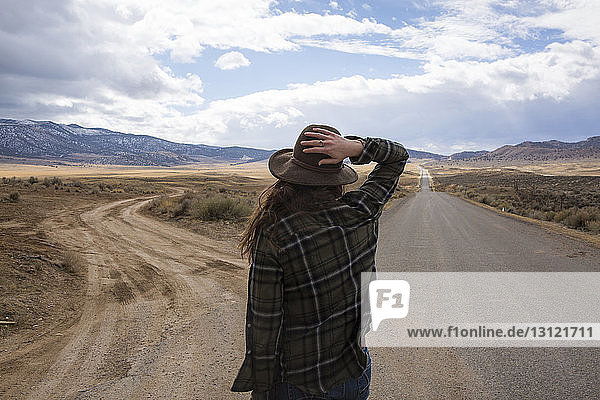 Rear view of woman wearing hat while standing on road against cloudy sky at Bryce Canyon National Park