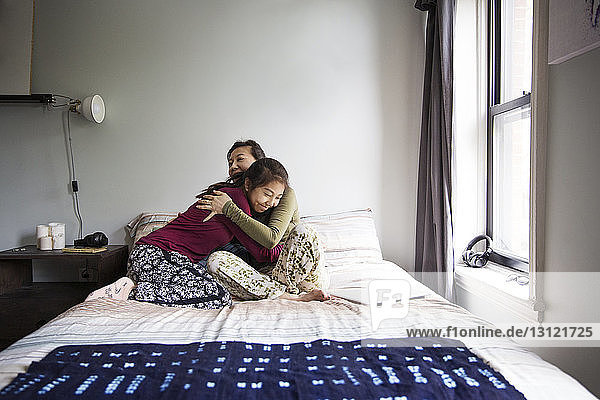 Mother embracing girl while sitting on bed at home