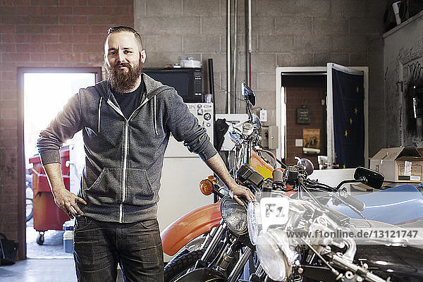 Portrait of confident mechanic standing by motorcycles at shop
