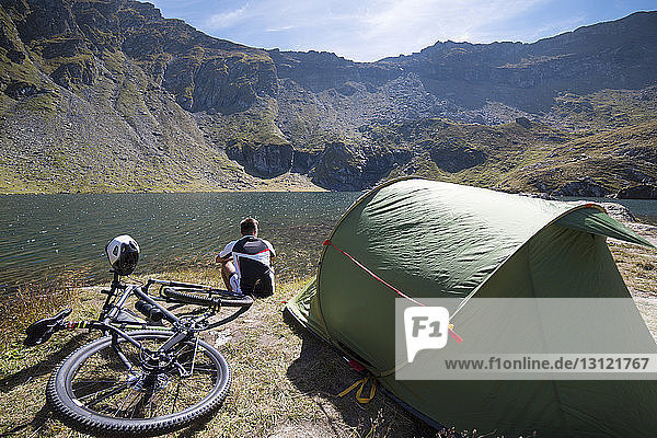 Rear view of athlete sitting by tent against lake