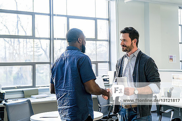 Businessmen doing handshake while standing in office