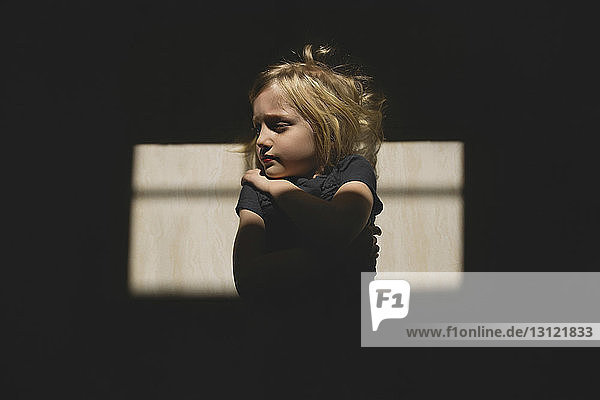 Thoughtful girl with arms crossed standing against wall during sunny day