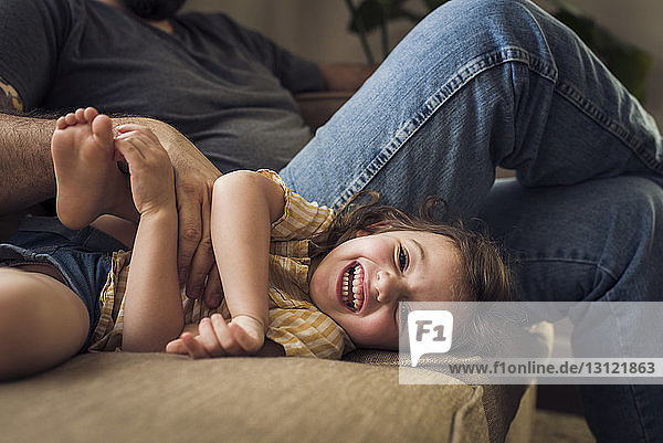Porträt eines fröhlichen Mädchens mit Vater  der zu Hause auf dem Sofa spielt