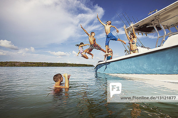 Children jumping from boat at sea against sky