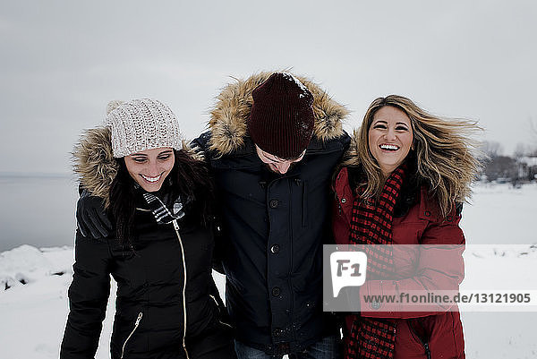 Glückliche Freunde stehen auf schneebedecktem Feld vor wolkigem Himmel