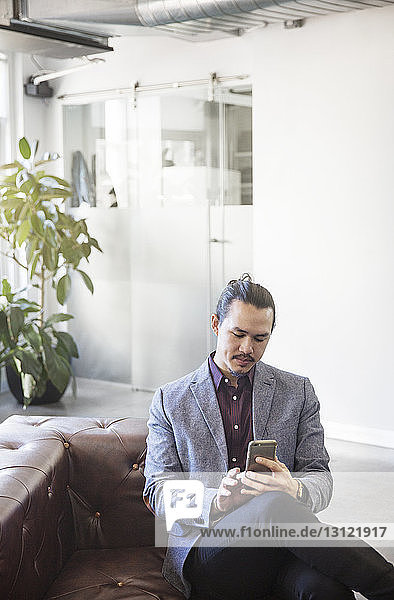 Man using mobile phone while sitting on sofa in office