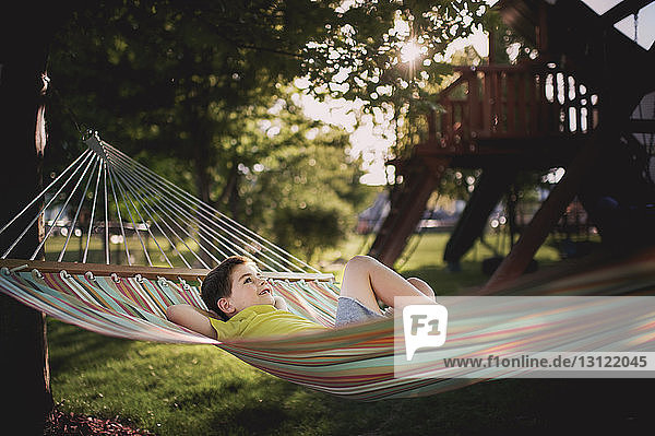Boy with hands behind head lying in hammock at park