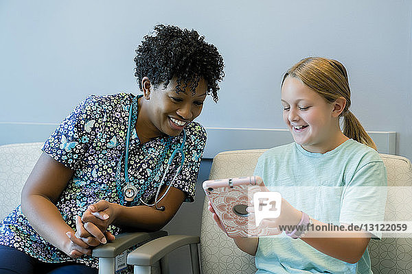 Fröhliches Mädchen zeigt einem Kinderarzt im Krankenhaus einen Tablet-Computer
