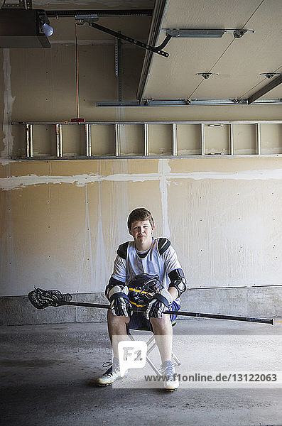 Porträt eines Mannes  der einen Lacrosse-Stick hält und auf einem Hocker sitzt