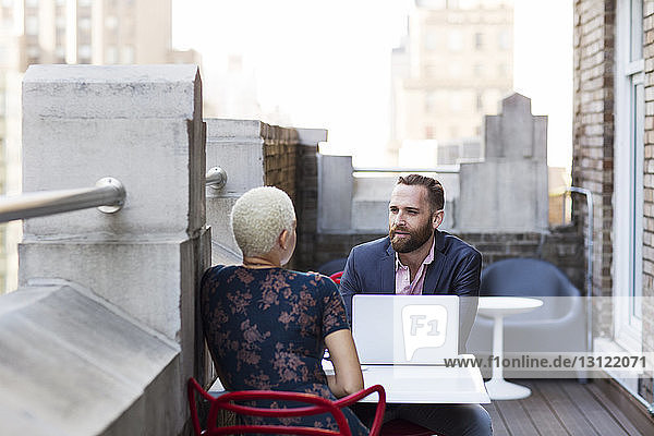 Mann benutzt Laptop-Computer während einer Diskussion mit einem Kollegen auf dem Balkon des Büros