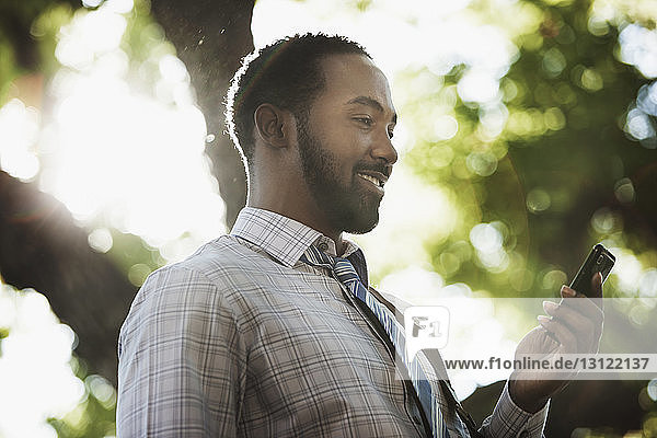 Lächelnder Mann hält Telefon  während er an einem sonnigen Tag steht