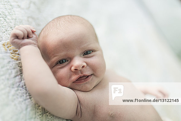 Portrait of shirtless smiling baby girl lying on bed at home