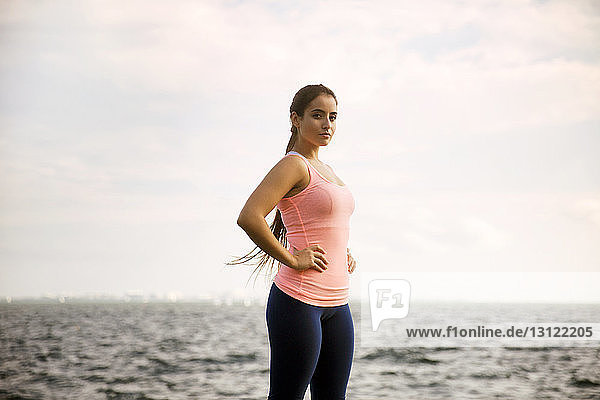 Portrait of confident woman standing against sea and cloudy sky