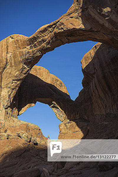 Mitteldistanzansicht einer Frau auf einer Felsformation im Arches-Nationalpark vor klarem blauen Himmel