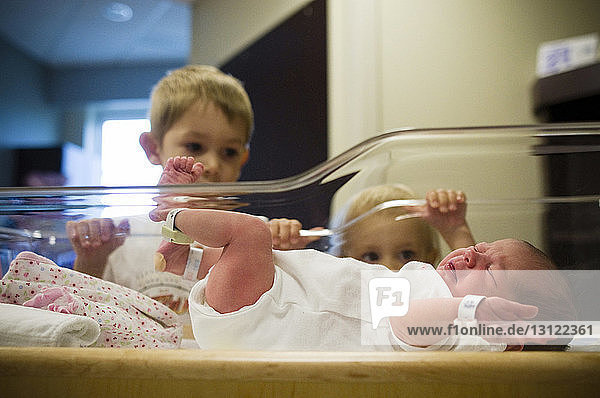 Geschwister sehen Neugeborene weinend in der Krippe im Krankenhaus